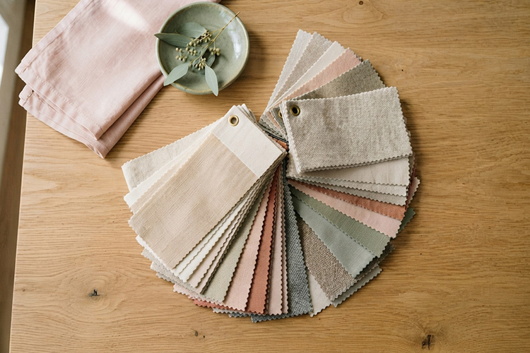 Free fabric swatches for handmade beds fanned out on an oak table in cream, sage and blush tones